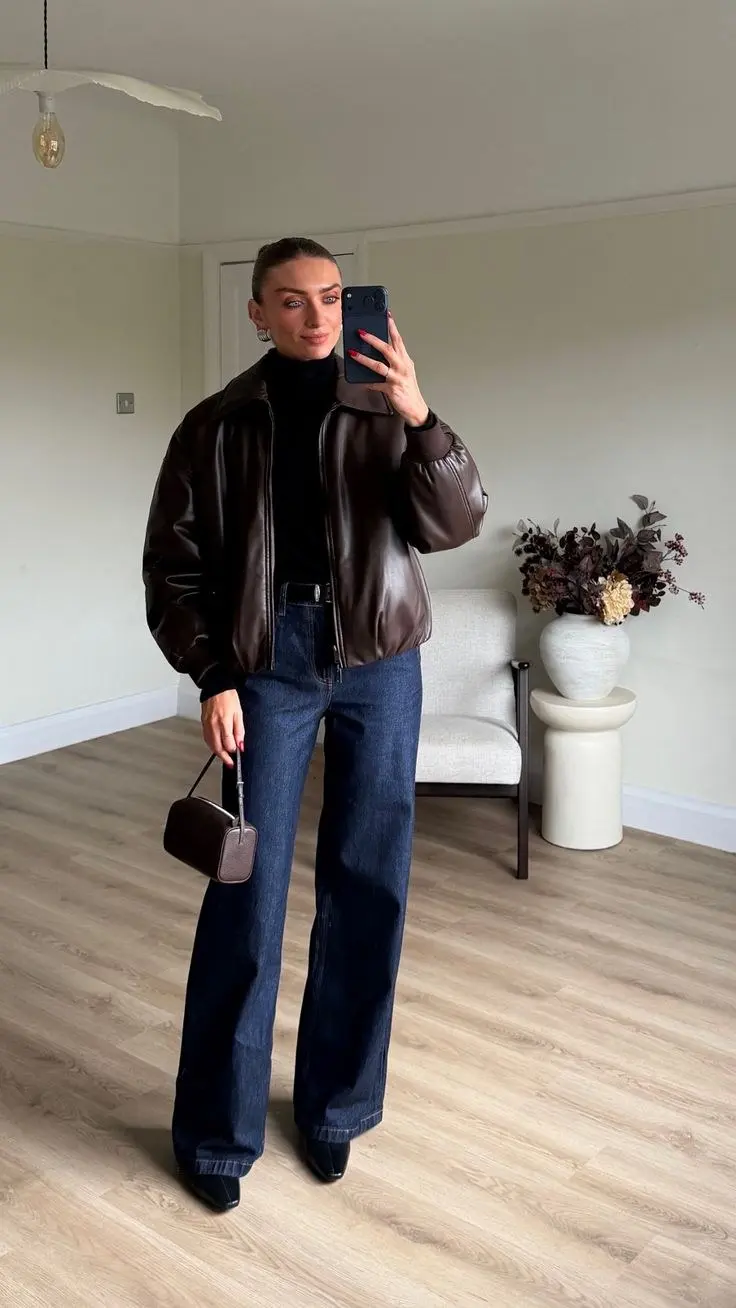woman in brown leather bomber jacket black turtleneck dark indigo wide leg jeans pointed black boots brown mini bag mirror selfie outfit 3