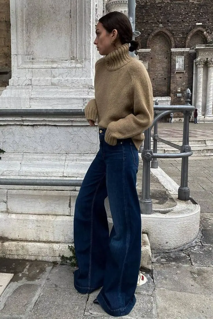 woman in camel chunky turtleneck knit dark navy wide leg jeans with front seam detail low bun white sneakers cobblestone background outfit 12