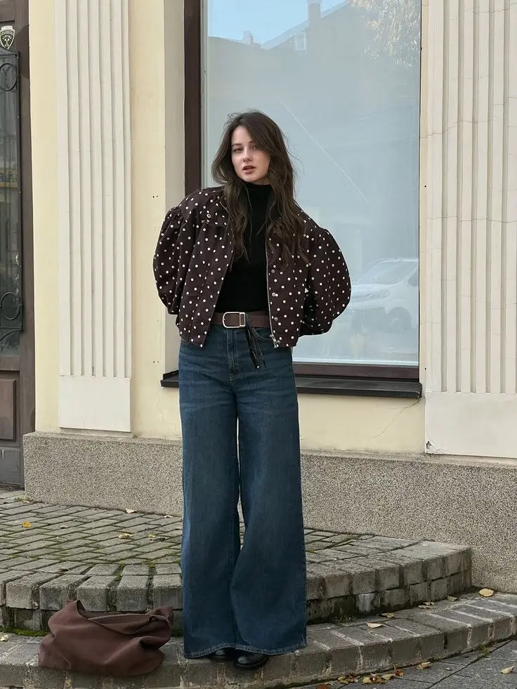 woman in brown white polka dot puff sleeve bomber jacket black turtleneck dark blue wide leg jeans brown leather belt black ankle boots brown suede bag street outfit 15