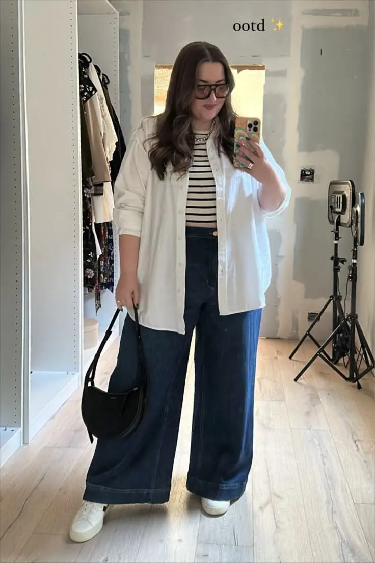 plus size woman in white oversized shirt open over striped t-shirt dark indigo wide leg jeans white sneakers black crescent shoulder bag large sunglasses mirror selfie outfit 20