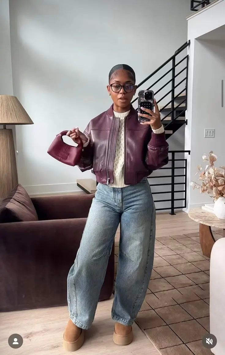 woman in burgundy leather bomber jacket cable knit sweater light wash barrel jeans platform UGGs and burgundy mini bag mirror selfie outfit 1