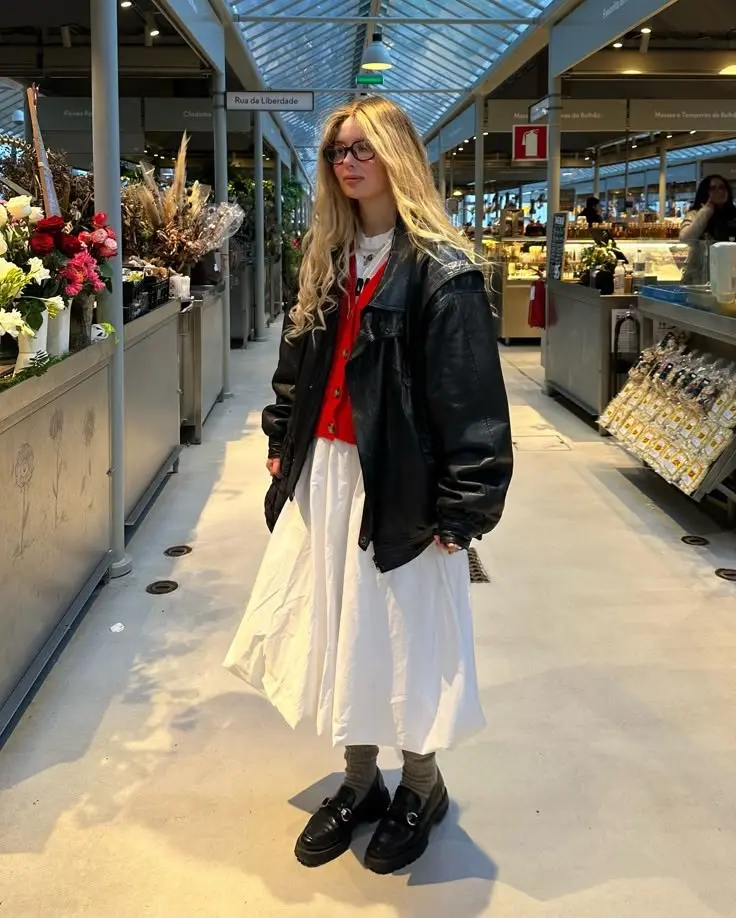 woman in oversized black leather jacket red button cardigan white maxi skirt chunky black loafers grey socks indoor market outfit 5