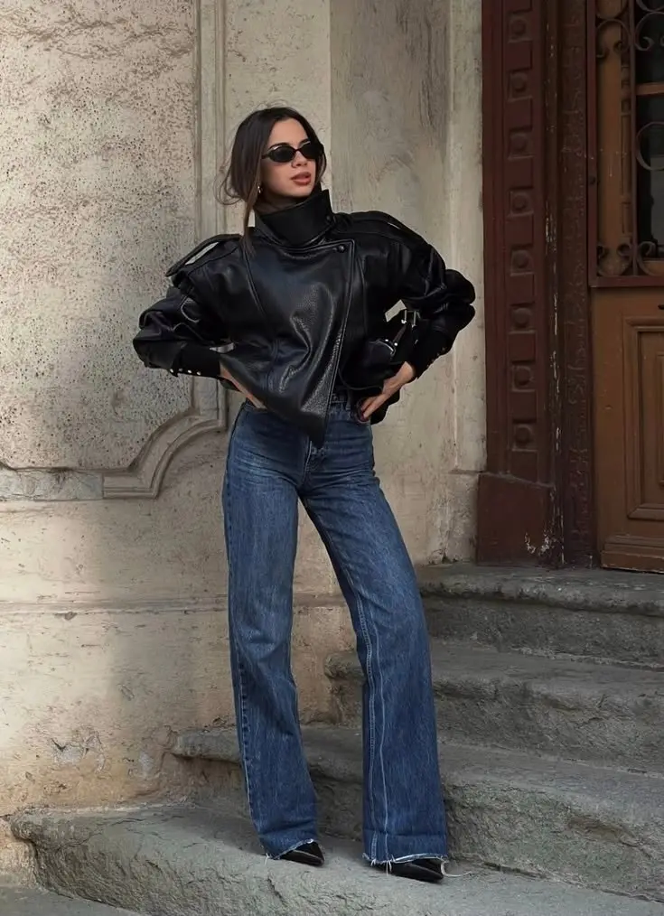 woman in black cropped moto leather jacket black turtleneck dark indigo wide leg jeans black pointed heels small sunglasses standing on steps outdoor outfit 9