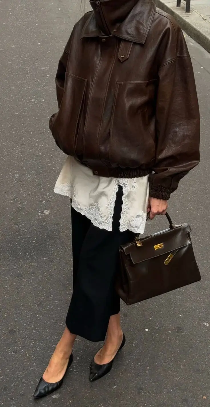 woman in chocolate brown vintage leather bomber jacket white lace hem slip top black wide leg trousers black pointed flats dark brown structured top handle bag street outfit 10