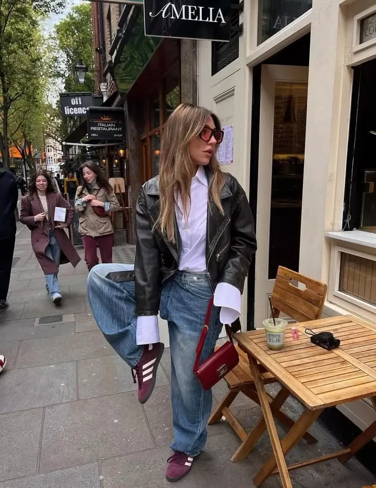 woman in black moto leather jacket white oxford shirt light blue wide leg jeans burgundy sneakers burgundy crossbody bag street cafe outdoor outfit 13