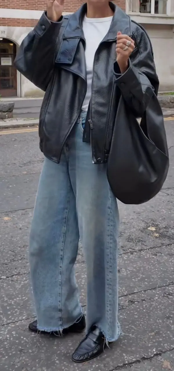 woman in slightly oversized black moto leather jacket white tee light blue barrel jeans black penny loafers large black leather hobo bag street outfit 16
