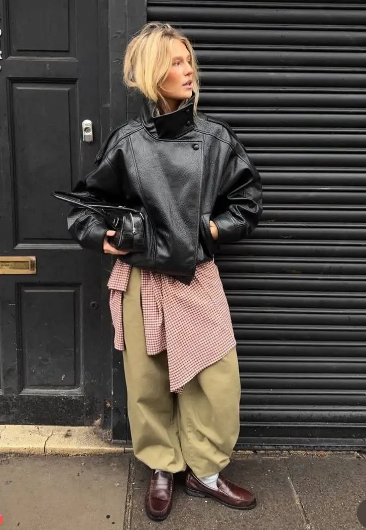 woman in black wide collar moto jacket gingham shirt tied at waist khaki balloon trousers burgundy chunky loafers white socks small black bag street style outfit 17