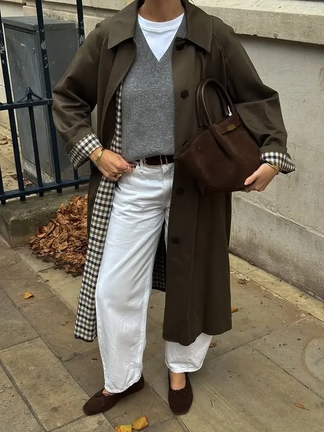 woman wearing olive green long trench coat over gray v-neck sweater gingham shirt white tee white straight jeans brown suede ballet flats brown suede bag outfit 3