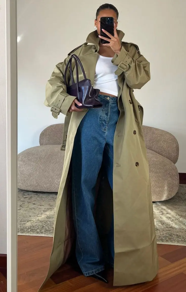 woman in mirror selfie wearing camel long trench coat open over white crop top straight blue jeans small dark purple structured bag black boots outfit 4
