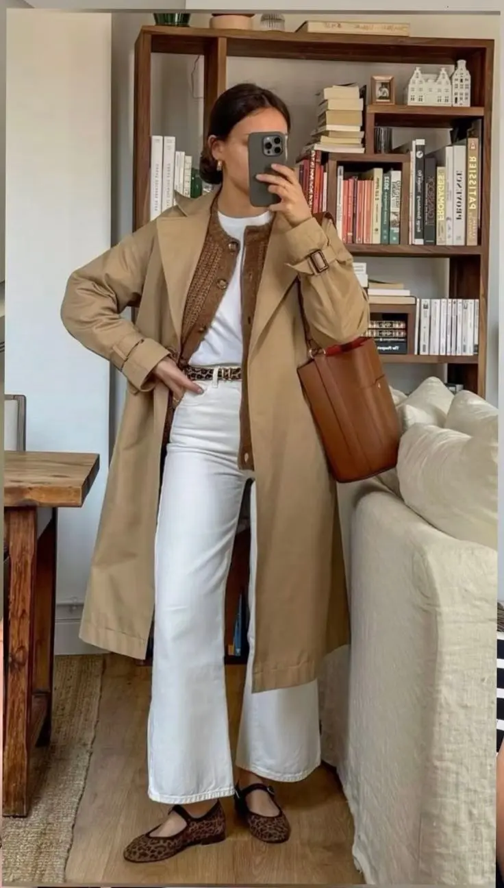 woman in mirror selfie wearing camel trench coat over brown woven button cardigan white tee white straight jeans leopard print ballet flats tan leather bucket bag leopard belt outfit 7