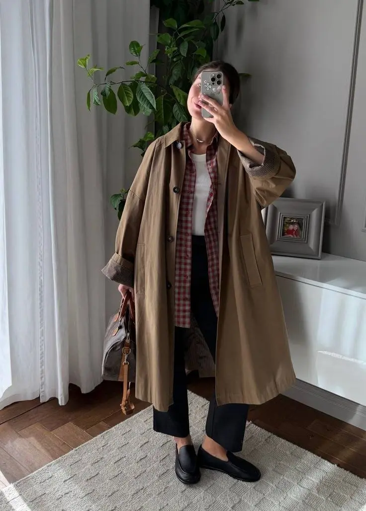 woman wearing beige long double-breasted trench coat over striped polo layered with white shirt straight blue raw hem jeans dark brown leather boat shoes dark leather tote bag sunglasses outfit 11