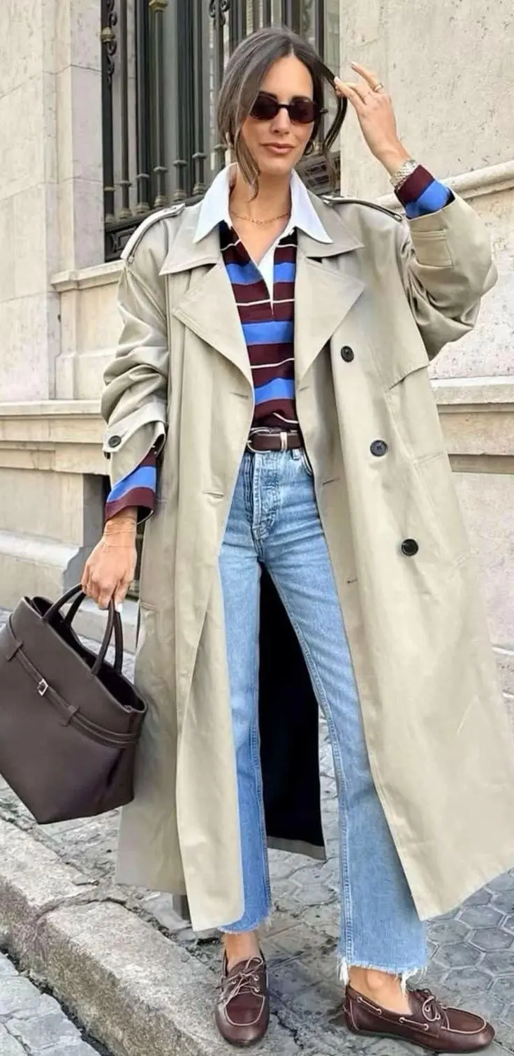 woman on street in beige long trench coat open over white tee wide leg blue jeans navy baseball cap woven brown shoulder bag gray white retro sneakers outfit 12