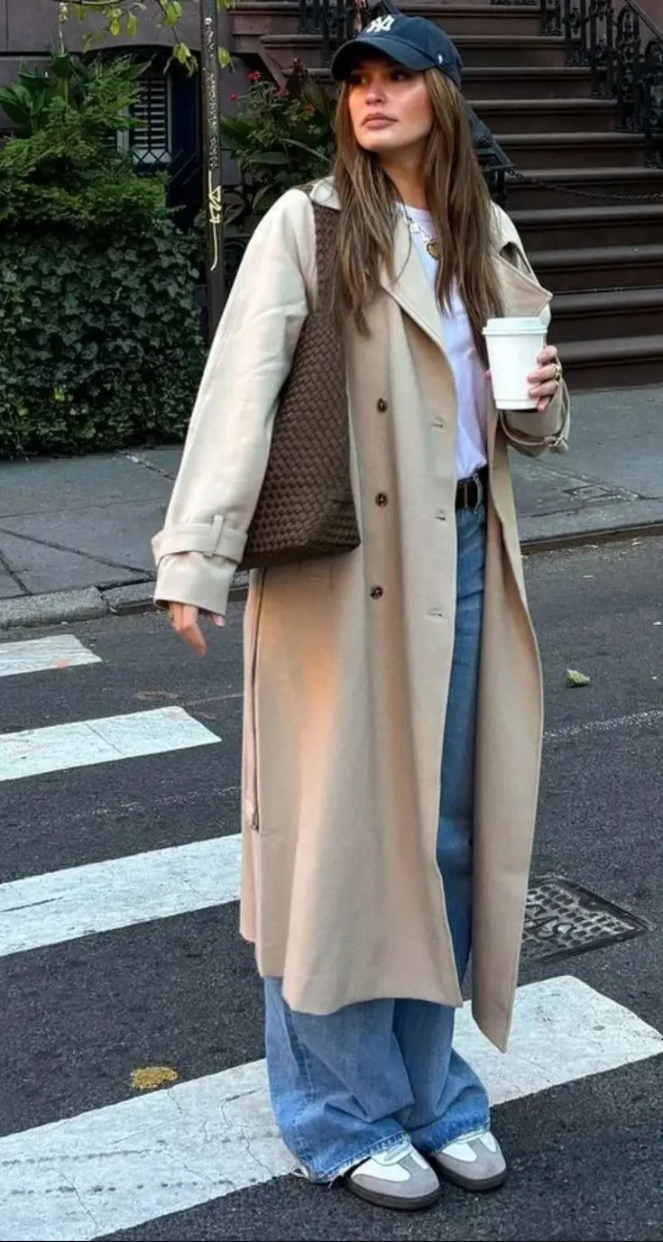 woman from behind walking wearing dark brown leather long trench coat flare dark blue jeans black leather beret black ankle boots black structured top handle bag outdoor fall setting outfit 13