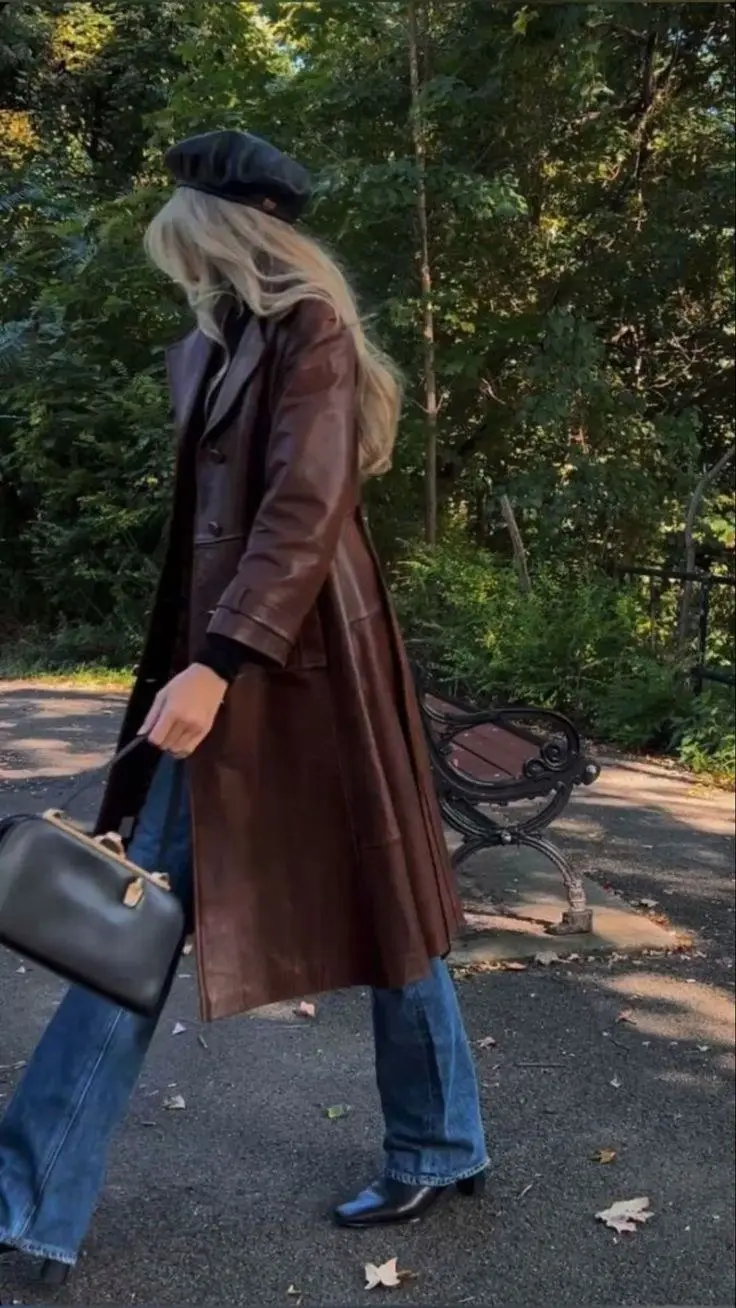 woman indoors wearing brown suede mid-length double-breasted trench coat black fitted top black wide leg trousers black pointed kitten heel boots black structured handbag outfit 14
