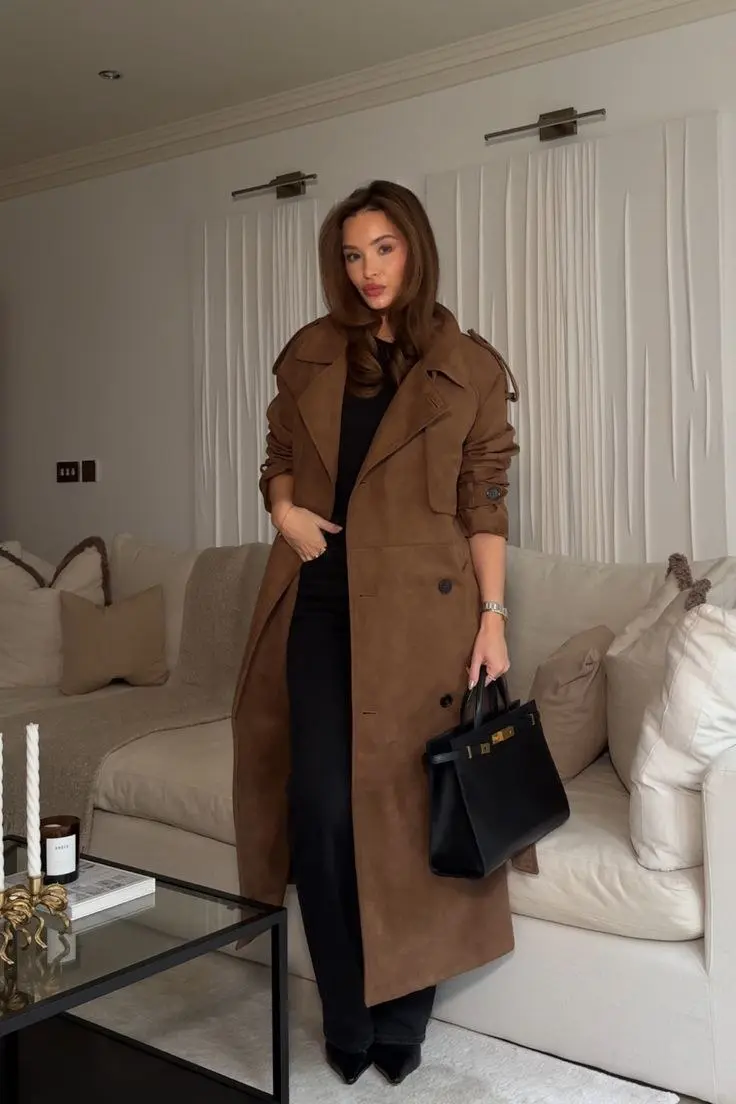 woman on street wearing beige balmacaan single button long trench coat over white silk shirt straight blue jeans brown heeled strappy sandals raffia woven shoulder bag gold hoop earrings low bun outfit 15