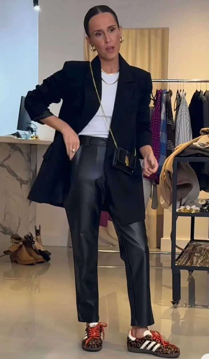 woman in store wearing oversized black blazer, white T-shirt, black leather straight-leg pants, leopard print sneakers, small black chain-strap mini bag, gold hoop earrings, slicked back hair, outfit 6
