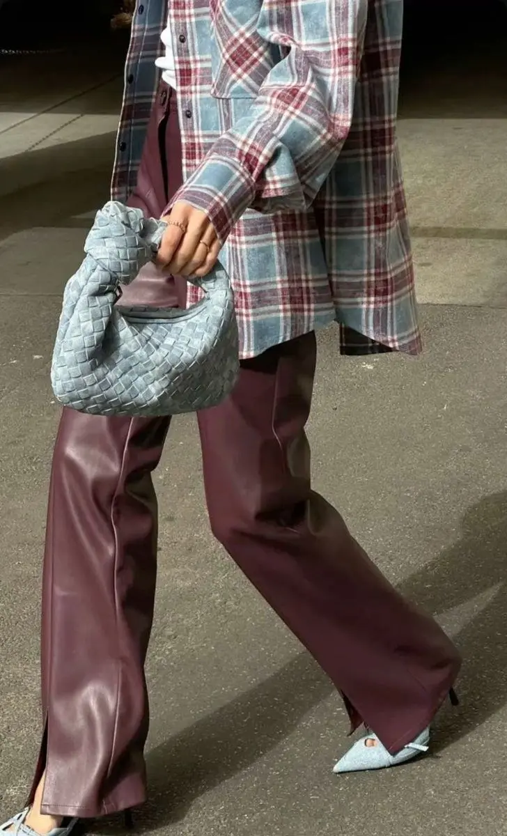close up street shot of woman wearing blue and red plaid oversized flannel shirt, burgundy-plum wide leg leather pants with side slit, blue crystal kitten heel pumps, light blue woven shoulder bag, outfit 11