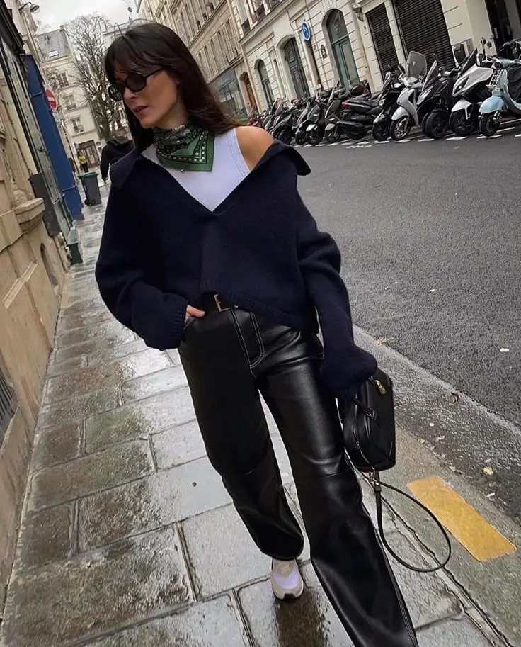 woman on wet city street wearing navy oversized off-shoulder V-neck knit sweater over white tank, green printed bandana tied at neck, black baggy leather pants, white sneakers, holding black leather structured bag, dark sunglasses, outfit 13