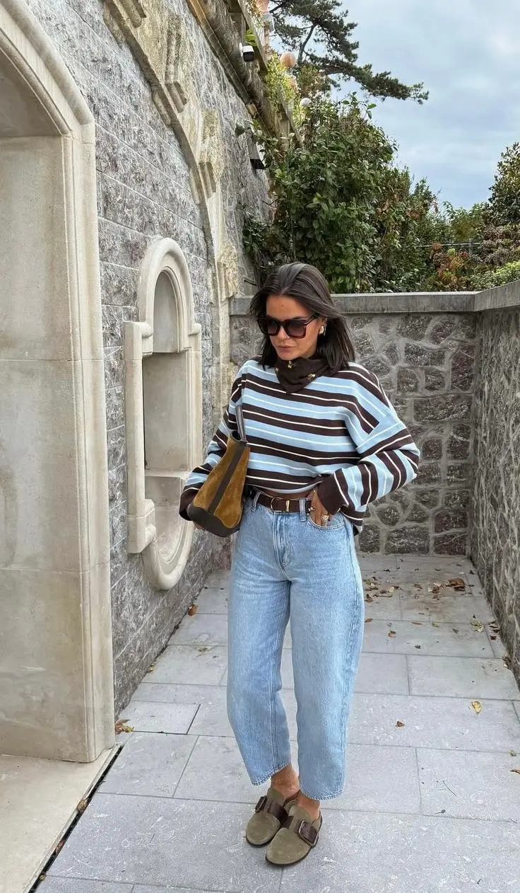 woman in blue and chocolate brown striped sweater over turtleneck barrel jeans suede bucket bag Birkenstock sandals sunglasses outdoor outfit 3