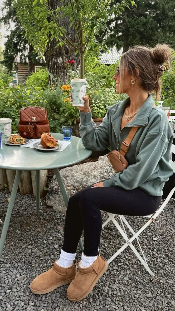 woman seated at outdoor cafe table in sage green quarter zip fleece black leggings white socks UGG mini boots tan belt bag gold jewelry outfit 4