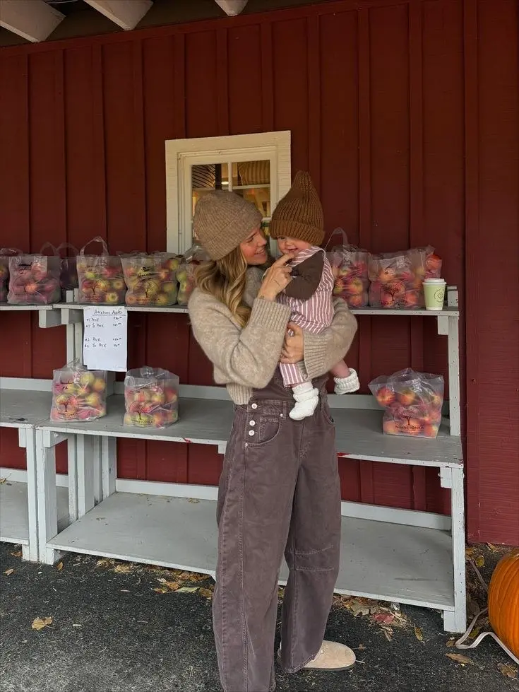 woman holding baby in camel ribbed knit sweater camel beanie dark mauve wide leg jeans UGG slides outside apple stand autumn outfit 7