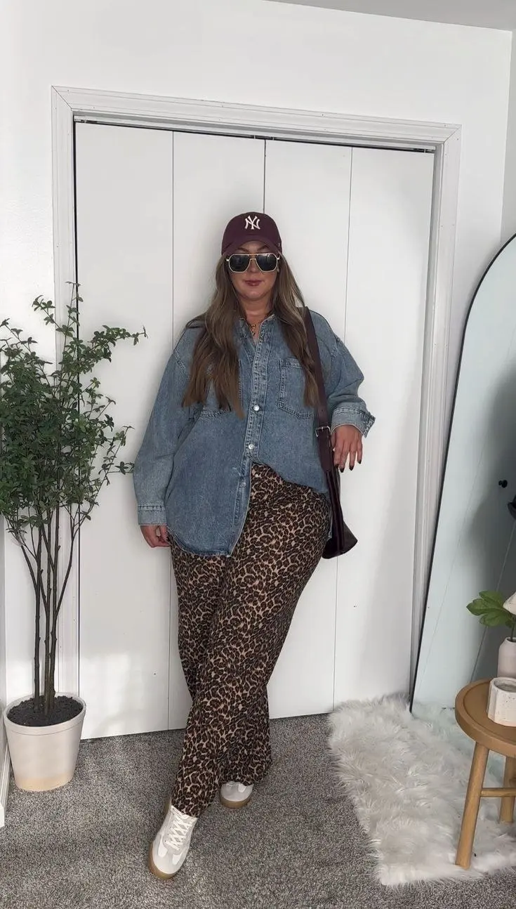 woman in oversized denim shirt open over leopard print wide leg pants white sneakers burgundy cap dark shoulder bag indoor outfit 9