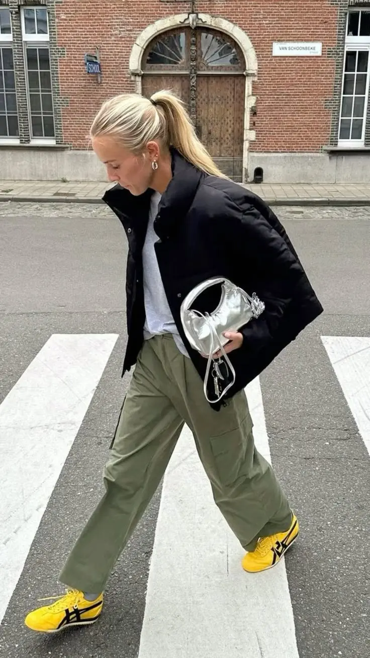 woman crossing street in black puffer vest grey crewneck sweatshirt wide olive cargo pants silver metallic mini bag yellow sneakers ponytail outfit 15