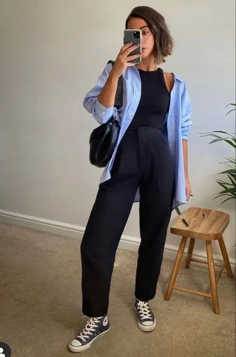 woman mirror selfie in oversized light blue oxford shirt open over black tank high waist black wide leg trousers black canvas high top sneakers black shoulder bag outfit 18