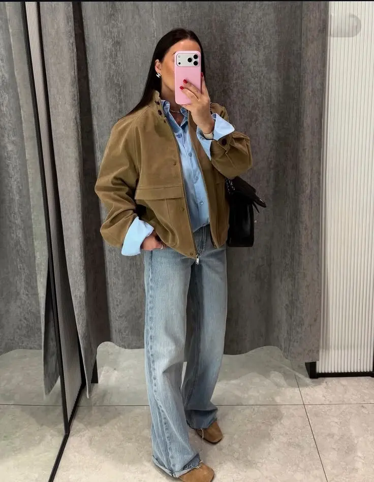 woman mirror selfie in tan brown suede zip jacket light blue denim shirt wide leg light jeans tan western boots small black bag gold jewelry outfit 21