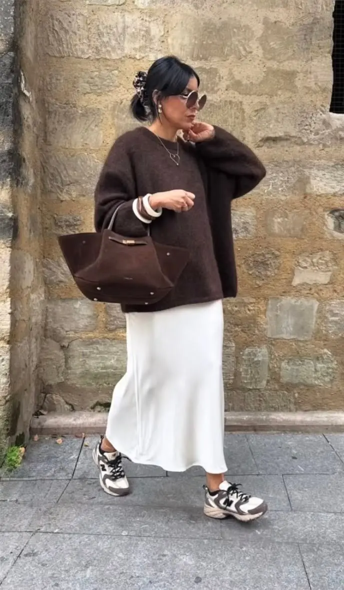 woman outdoors in chocolate brown oversized knit sweater cream satin midi slip skirt dark tan suede large tote chunky grey brown dad sneakers sunglasses hair clip outfit 24