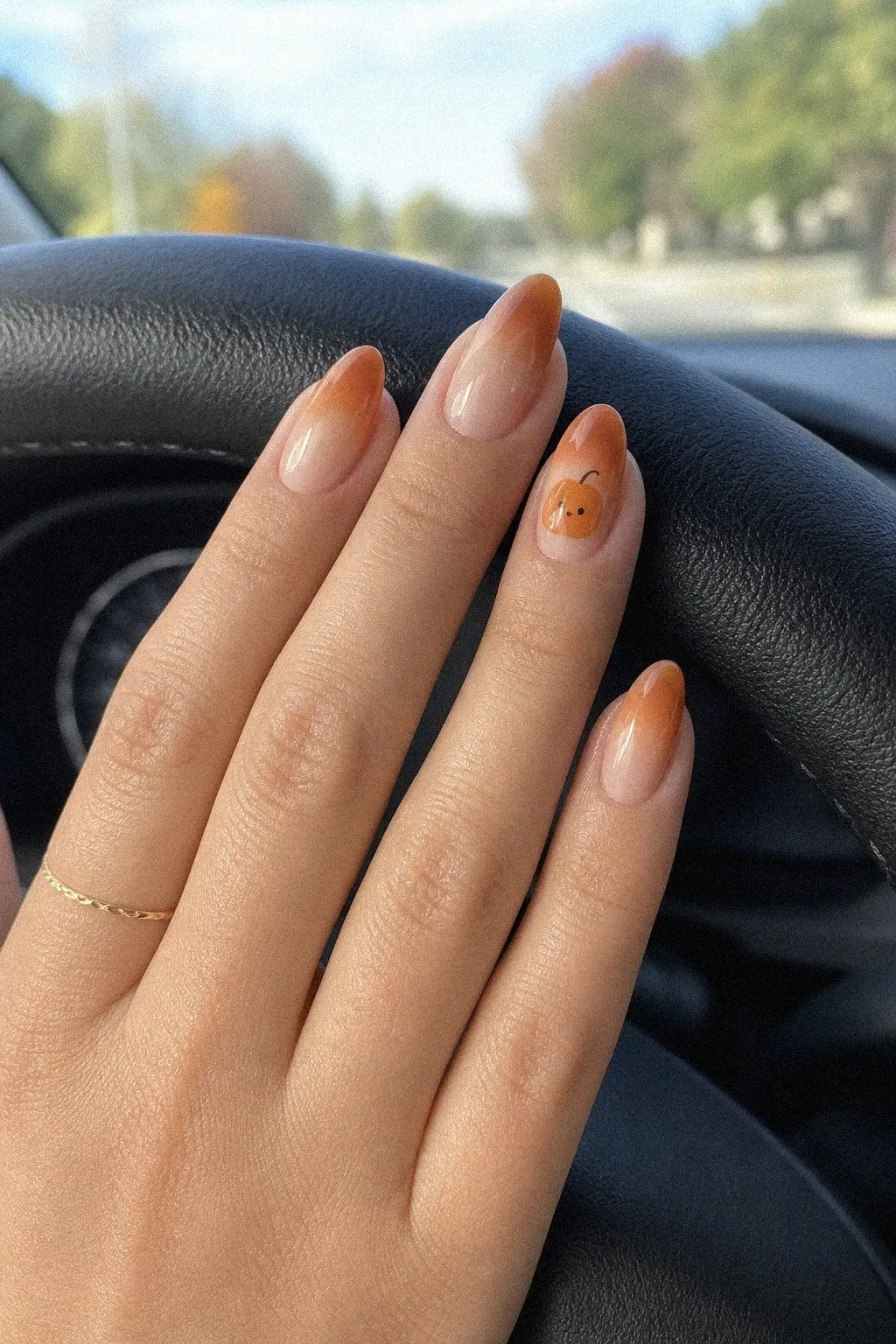 medium almond nails with caramel to nude ombre gel, single tiny orange pumpkin accent on ring finger, hand on car steering wheel, look 4
