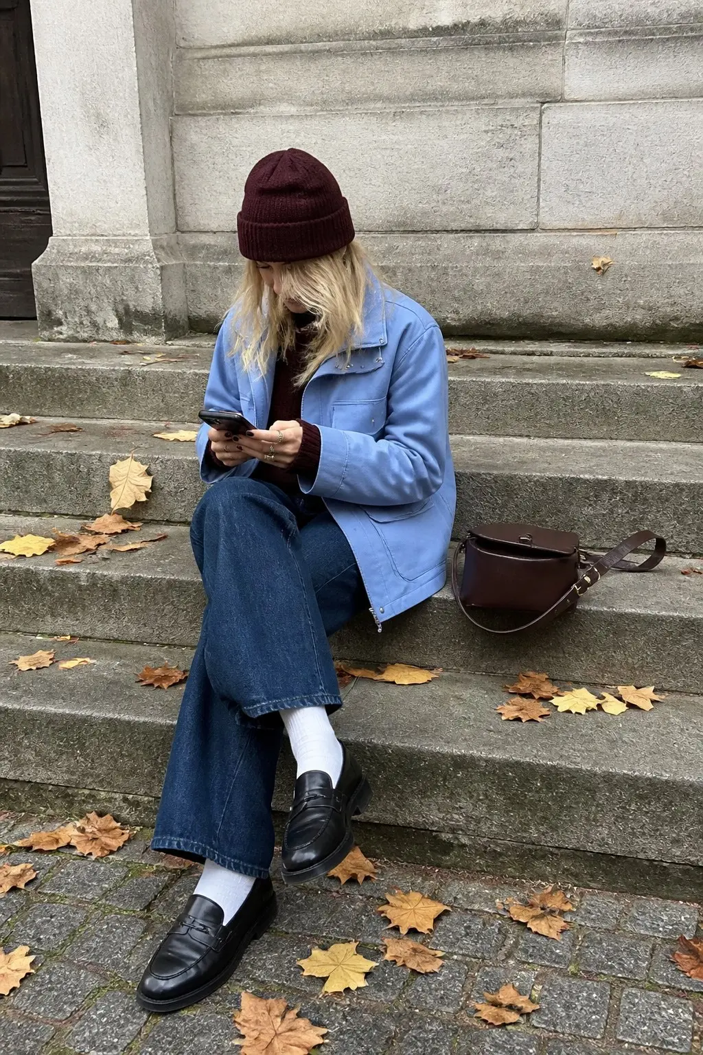 light blue utility jacket burgundy turtleneck knit dark wash wide leg jeans black penny loafers white crew socks burgundy beanie dark burgundy leather saddle crossbody bag outfit 25
