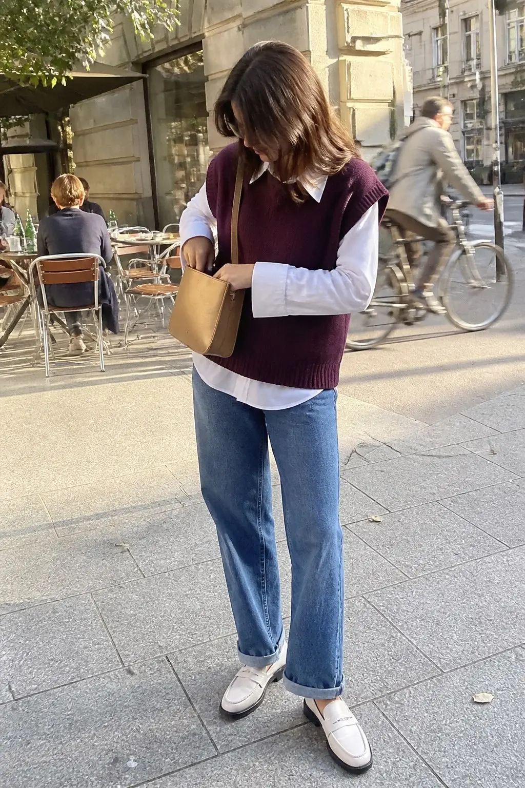 plum V-neck knit sweater vest over white collared shirt with straight-leg blue jeans white leather loafers and tan bucket bag outfit 7