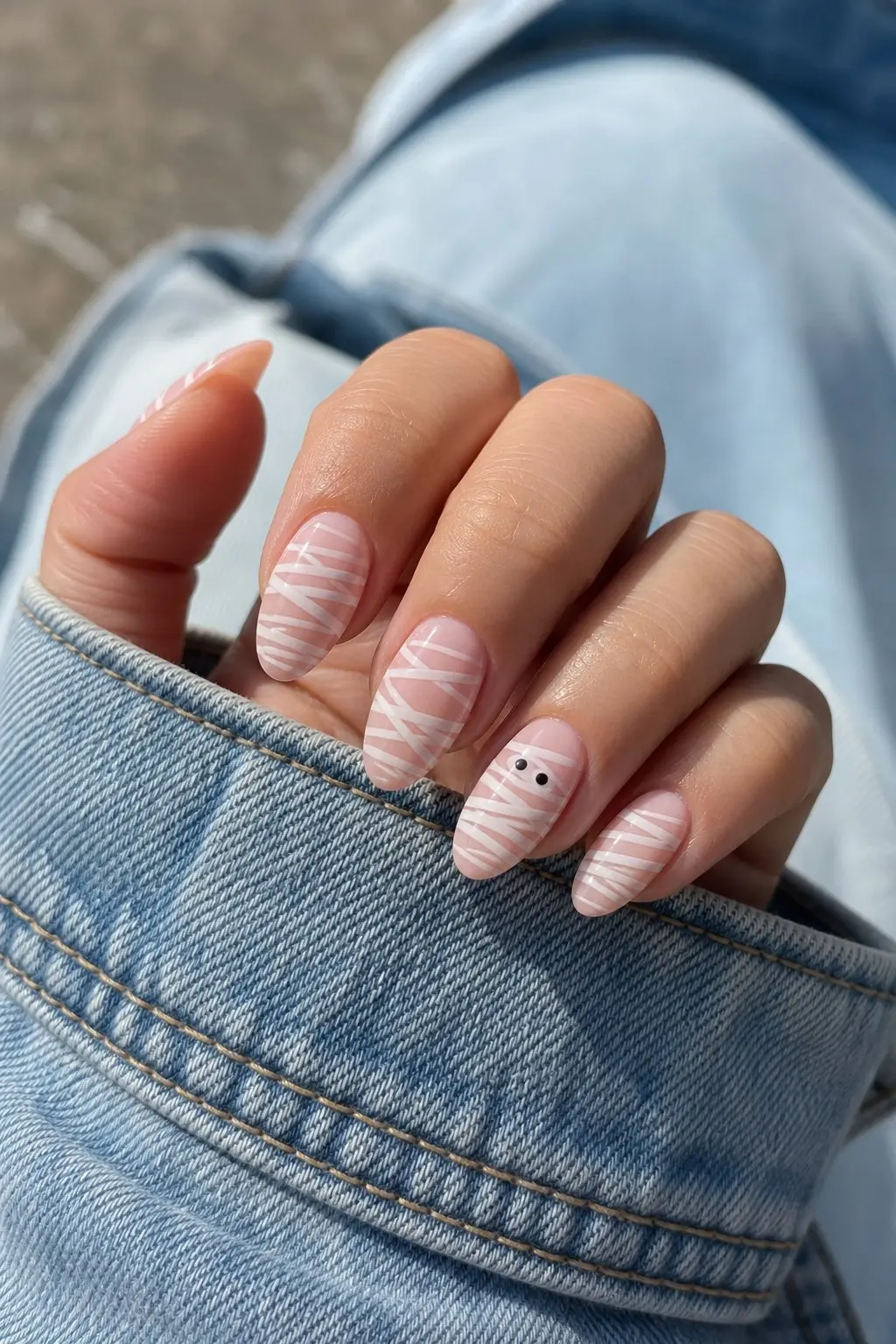 medium almond nails with warm blush gel base and white mummy wrap lines on all fingers, tiny black eyes on accent nail, glossy finish, nail look 2