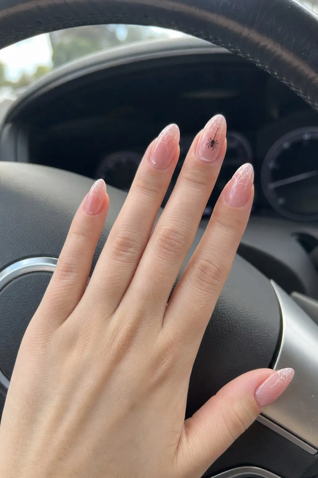 medium long almond nails with sheer baby pink base, white spider web French tip design on multiple nails, tiny black spider hanging on accent nail, nail look 4