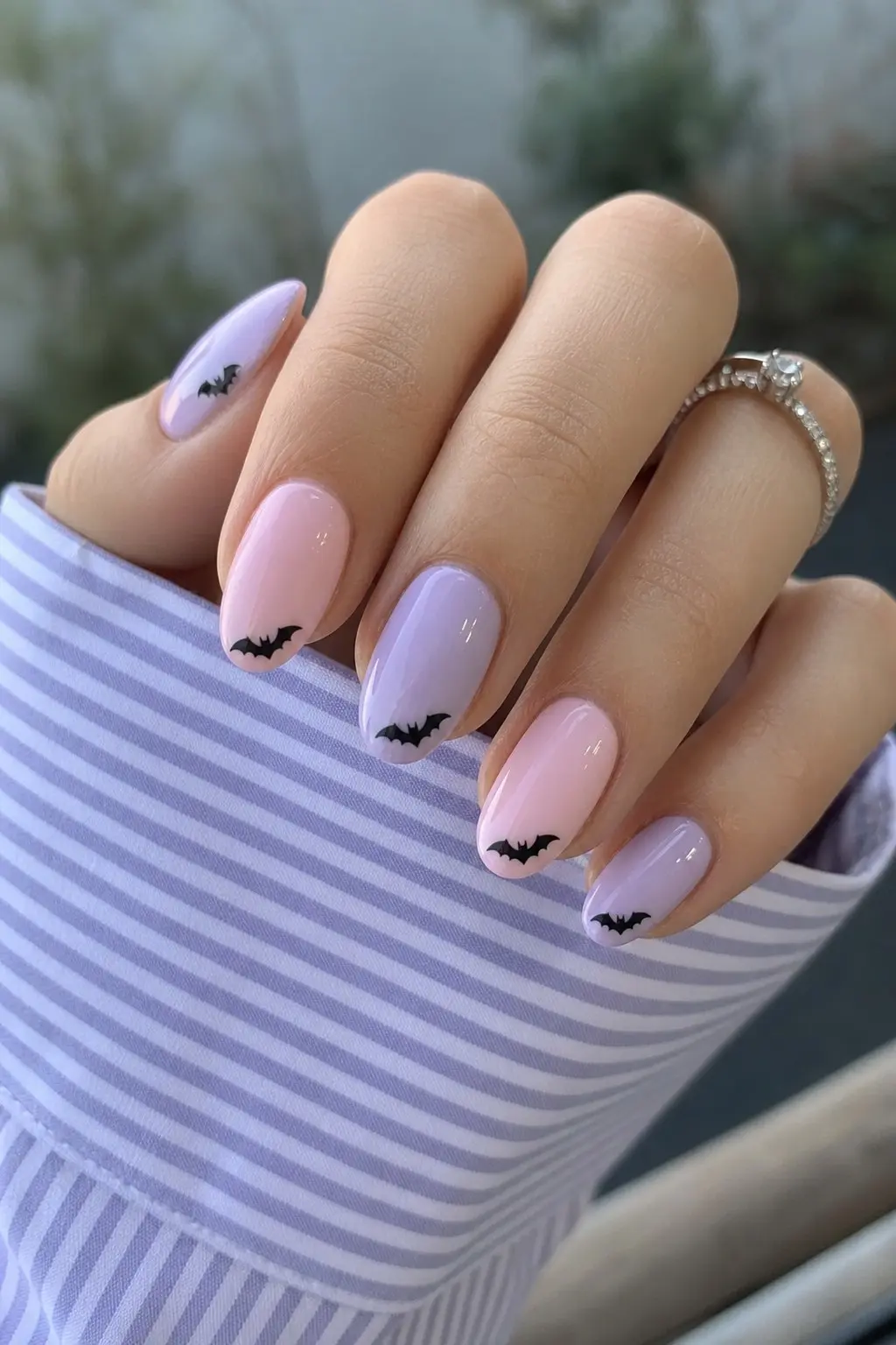 medium almond nails alternating baby pink and soft lilac gel polish, tiny black bat silhouettes stamped at lower nail tips on multiple nails, glossy finish, nail look 7