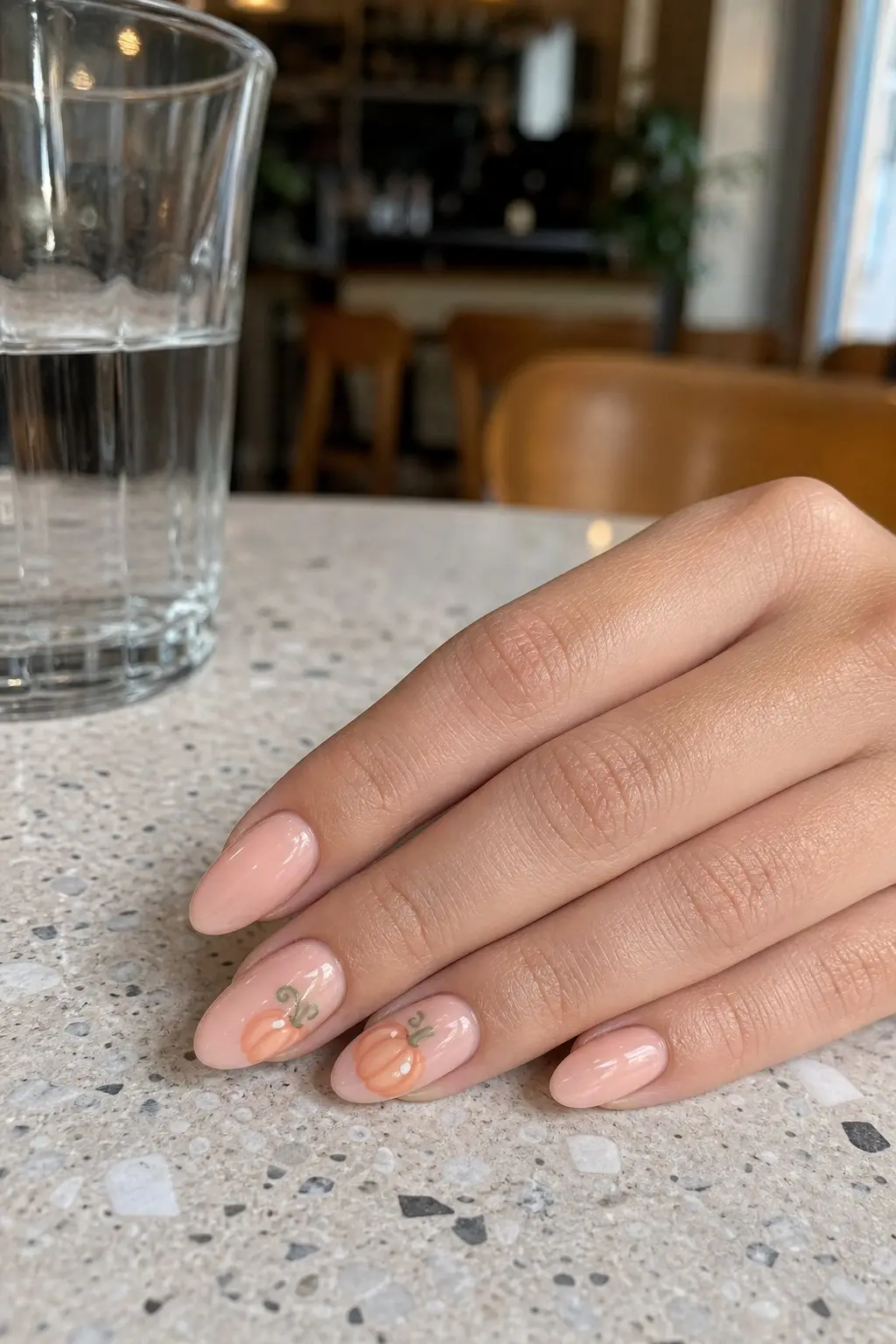medium almond nails with peach pink gel base, hand-painted pastel orange mini pumpkins with green curling stems on two accent nails, remaining nails plain peach pink, nail look 8