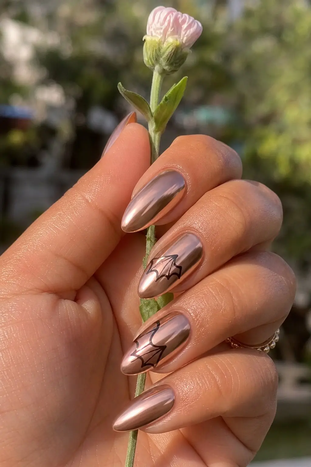 medium almond nails with rose gold chrome mirror finish base, black bat wing outline painted on two accent nails, nail look 9