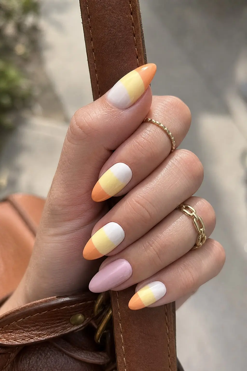 medium almond nails with white base, pastel yellow mid band and orange tip color block candy corn design on most nails, solid pink accent nail, nail look 10