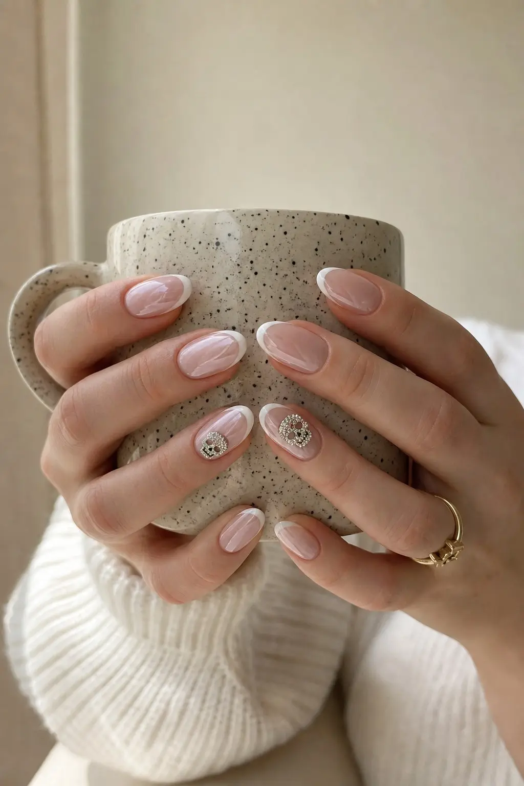 medium almond nails with nude sheer pink gel base and white French tip, semi-sheer swirl marble detail on some nails, rhinestone skull charm on one accent nail, gold ring, nail look 23