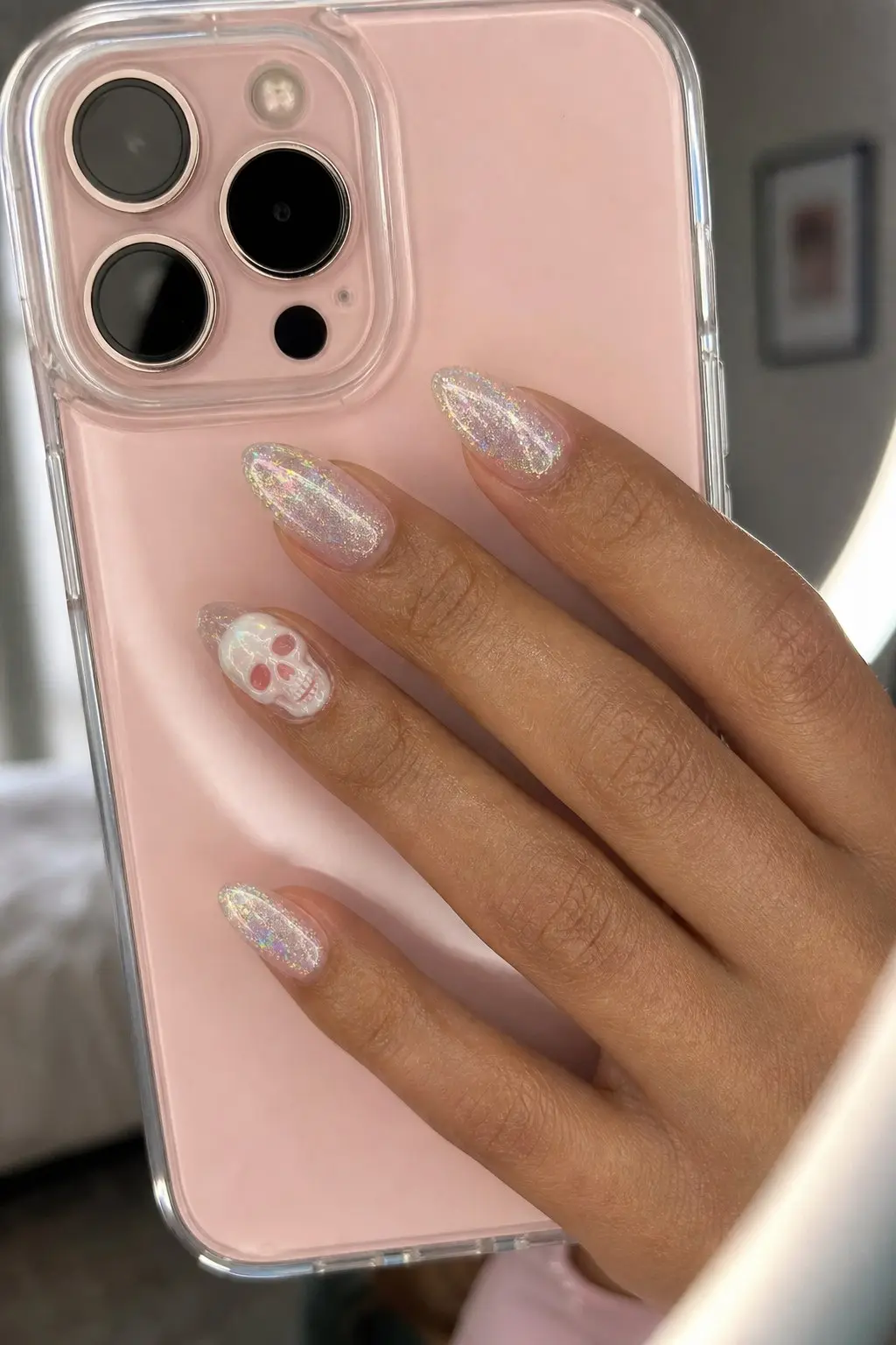 medium almond nails with holographic iridescent glitter gel base on all nails, accent nail features a 3D white skull with pink eye details, nail look 25