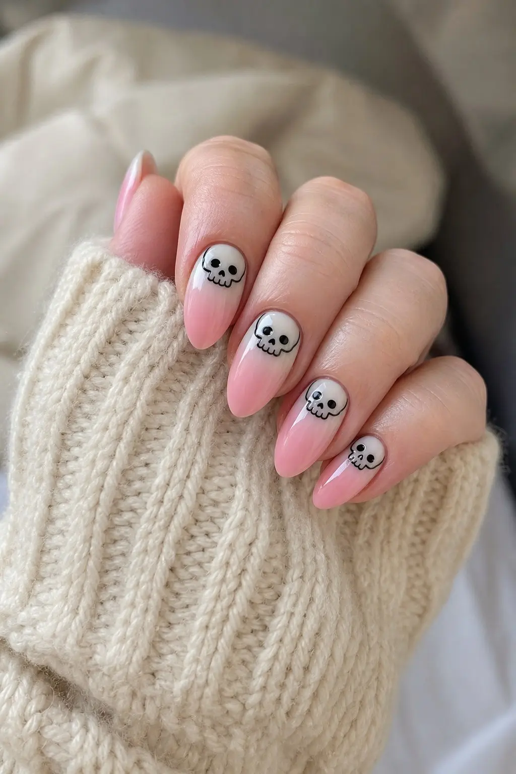 medium almond nails with pink to white ombre base and small black cartoon skull outline sitting at the base of each nail, nail look 26