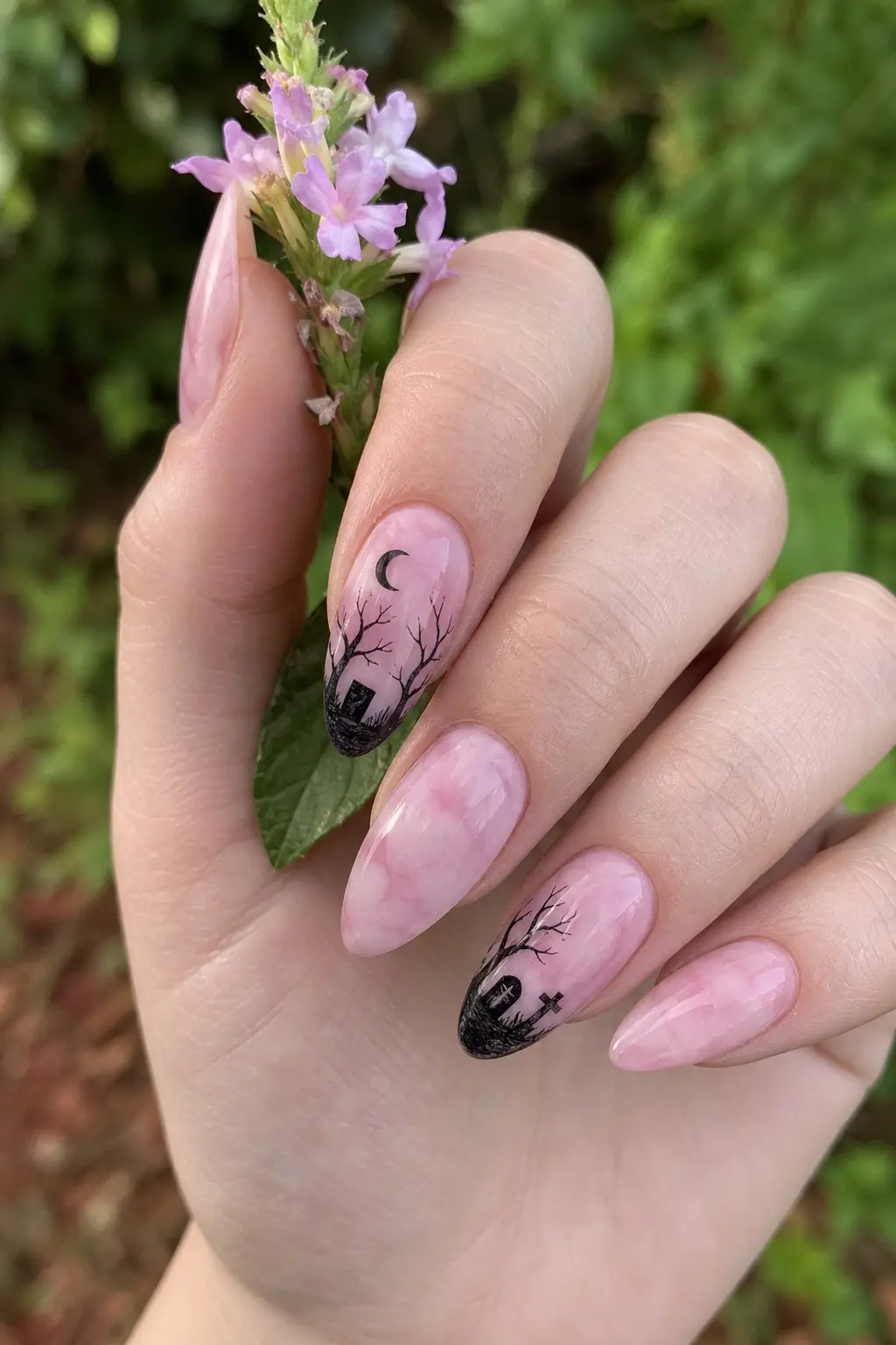 medium almond nails with pink marble swirl gel base, black graveyard silhouette with tombstone cross bare branches and crescent moon on two accent nails, remaining nails plain pink marble, nail look 29