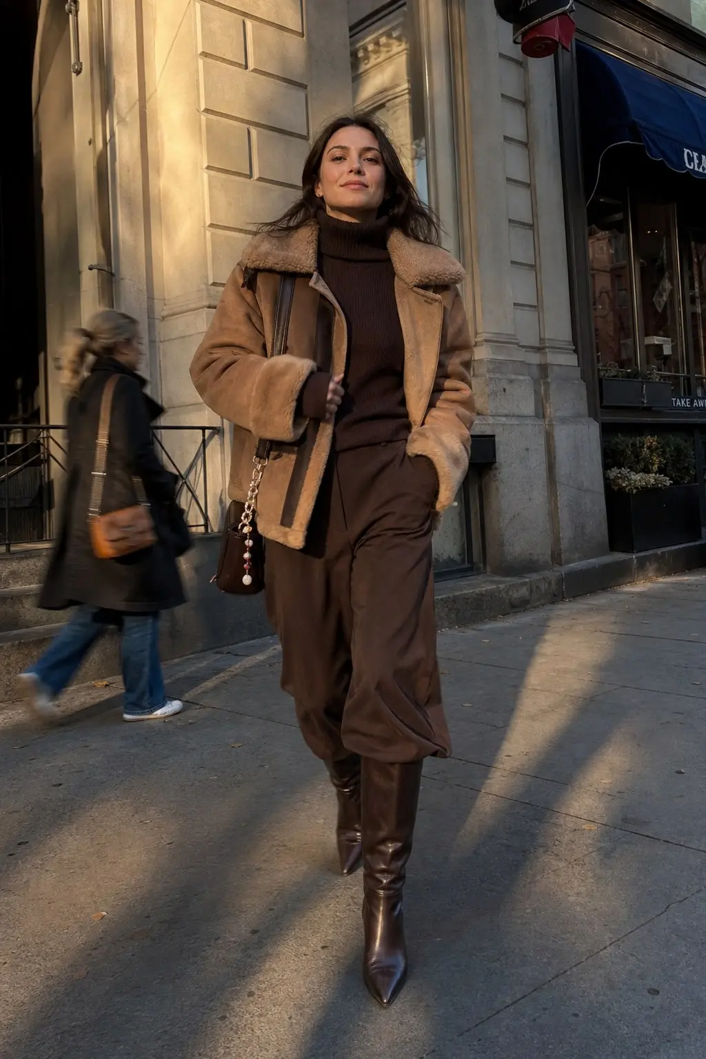 woman in dark brown ribbed turtleneck sweater dark brown wide leg trousers caramel shearling aviator jacket dark brown pointed knee high leather boots small dark brown bag chain strap outfit 2