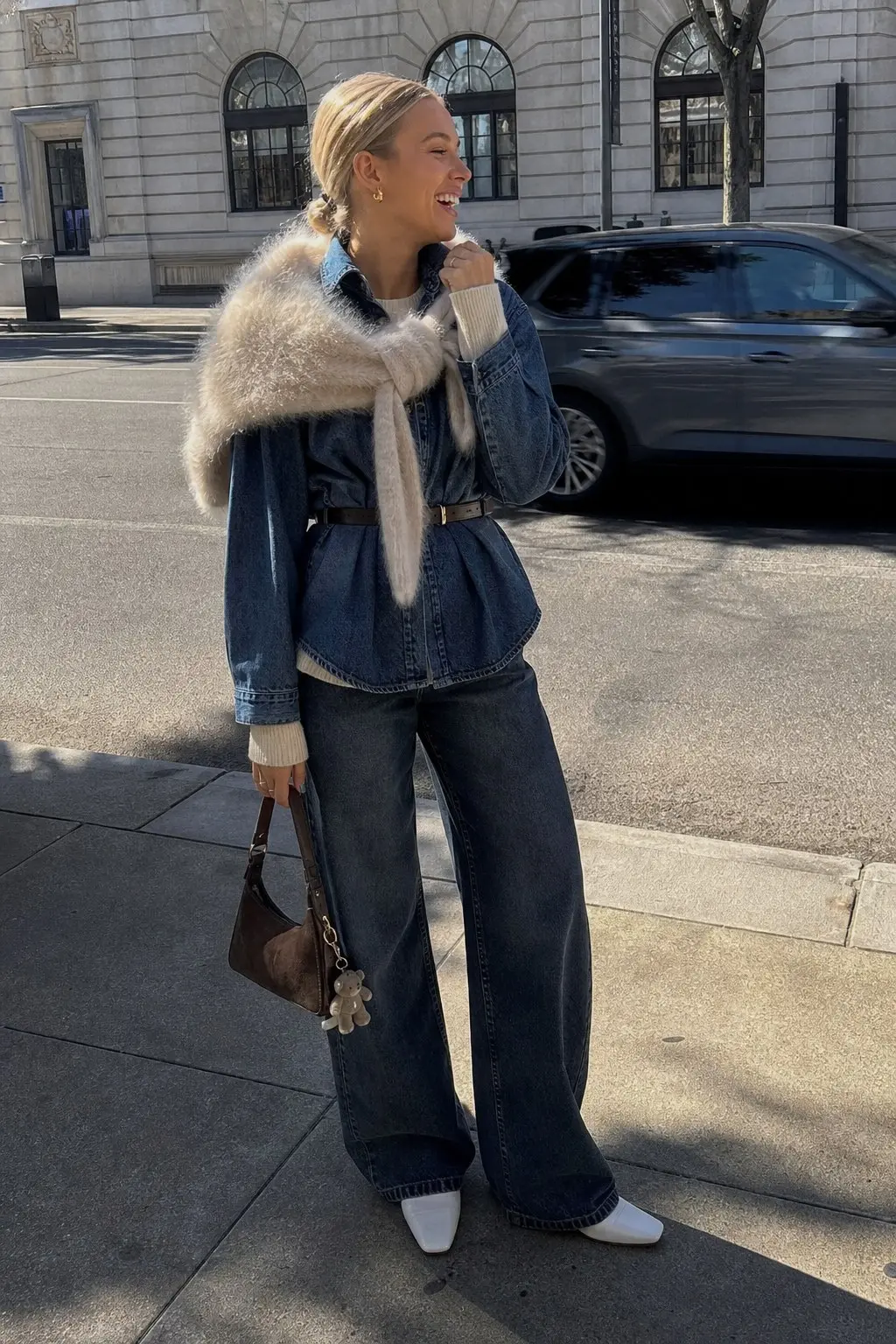 woman in dark navy wide leg jeans belted denim shirt jacket cream ribbed knit underneath cream fluffy faux fur scarf stole white pointed toe mules slim brown belt dark brown suede shoulder bag bear keychain outfit 7