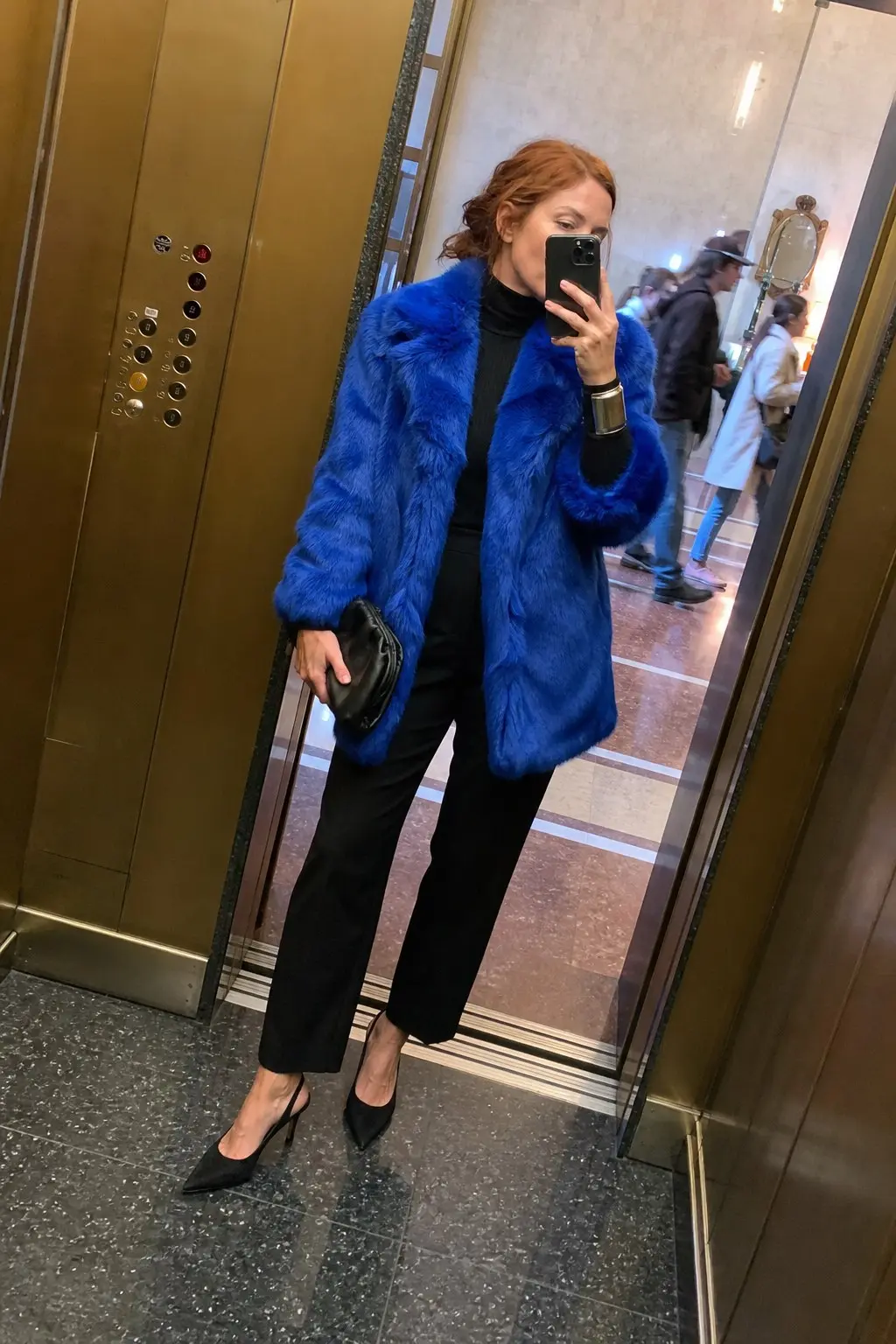 woman in electric blue faux fur coat black ribbed turtleneck black cropped straight leg trousers black pointed slingback heels silver cuff bracelet small black clutch bag outfit 9