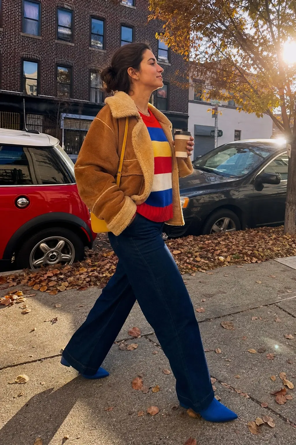 woman in tan shearling collar bomber jacket multicolor stripe knit sweater red yellow blue white color block dark indigo wide leg jeans cobalt blue suede ankle boots yellow crossbody bag outfit 21