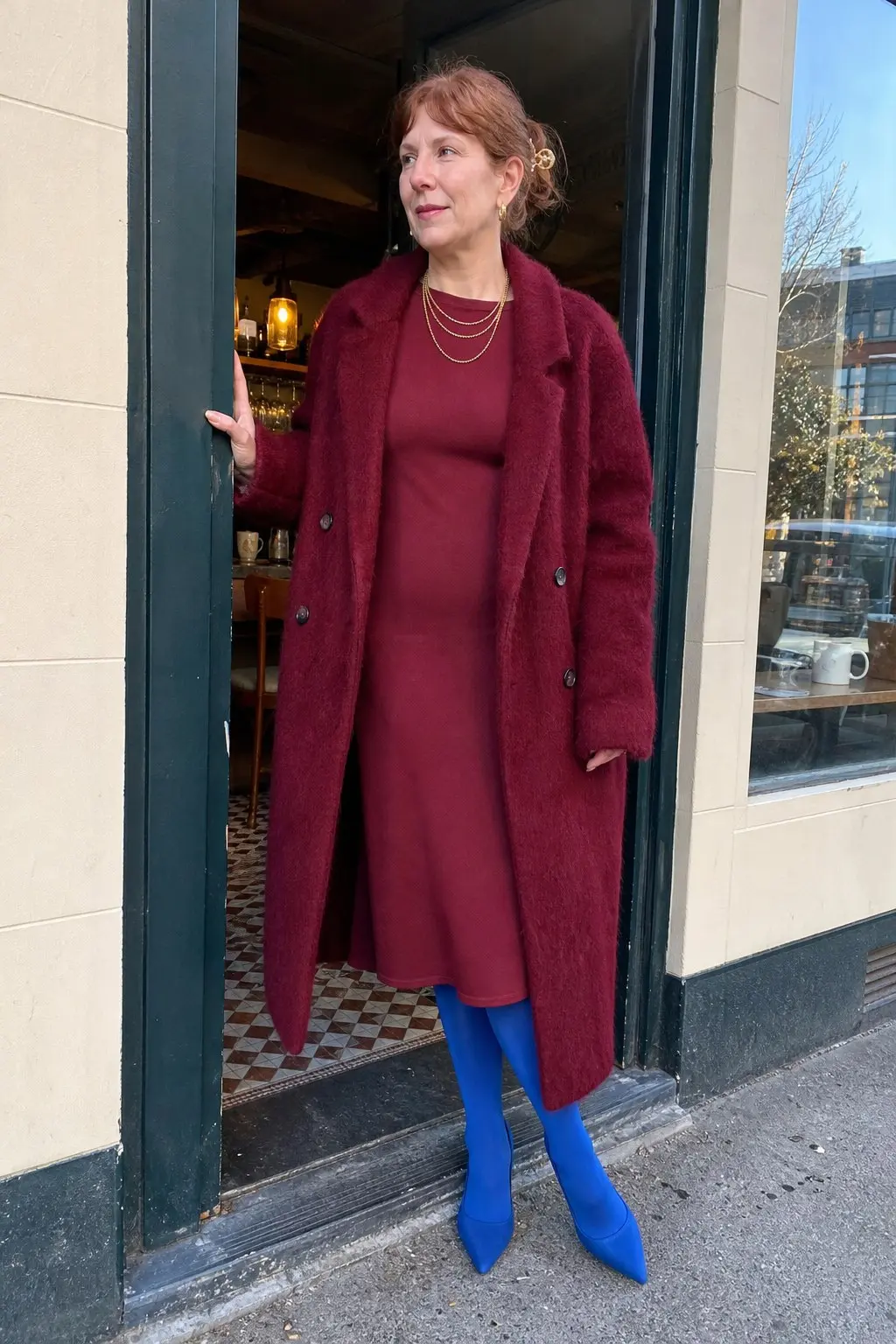 woman in longline burgundy fluffy oversized coat burgundy ribbed knit midi dress cobalt blue opaque tights cobalt blue pointed toe pumps layered gold chain necklaces gold hair clip outfit 23