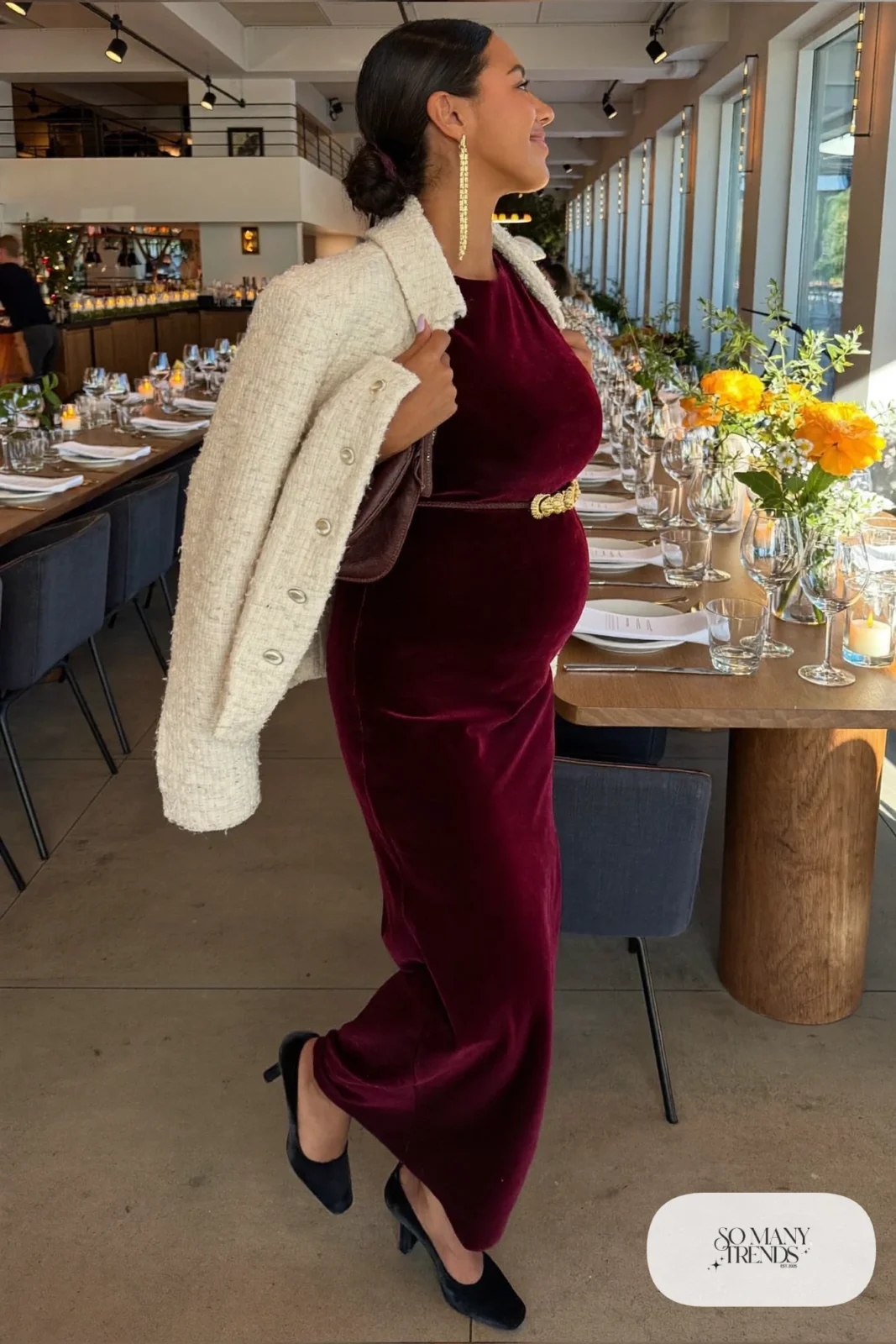 pregnant woman in deep burgundy long sleeve velvet maxi dress, thin gold belt above belly, gold drop earrings, black closed toe pumps, cream boucle jacket on shoulders, outfit 10