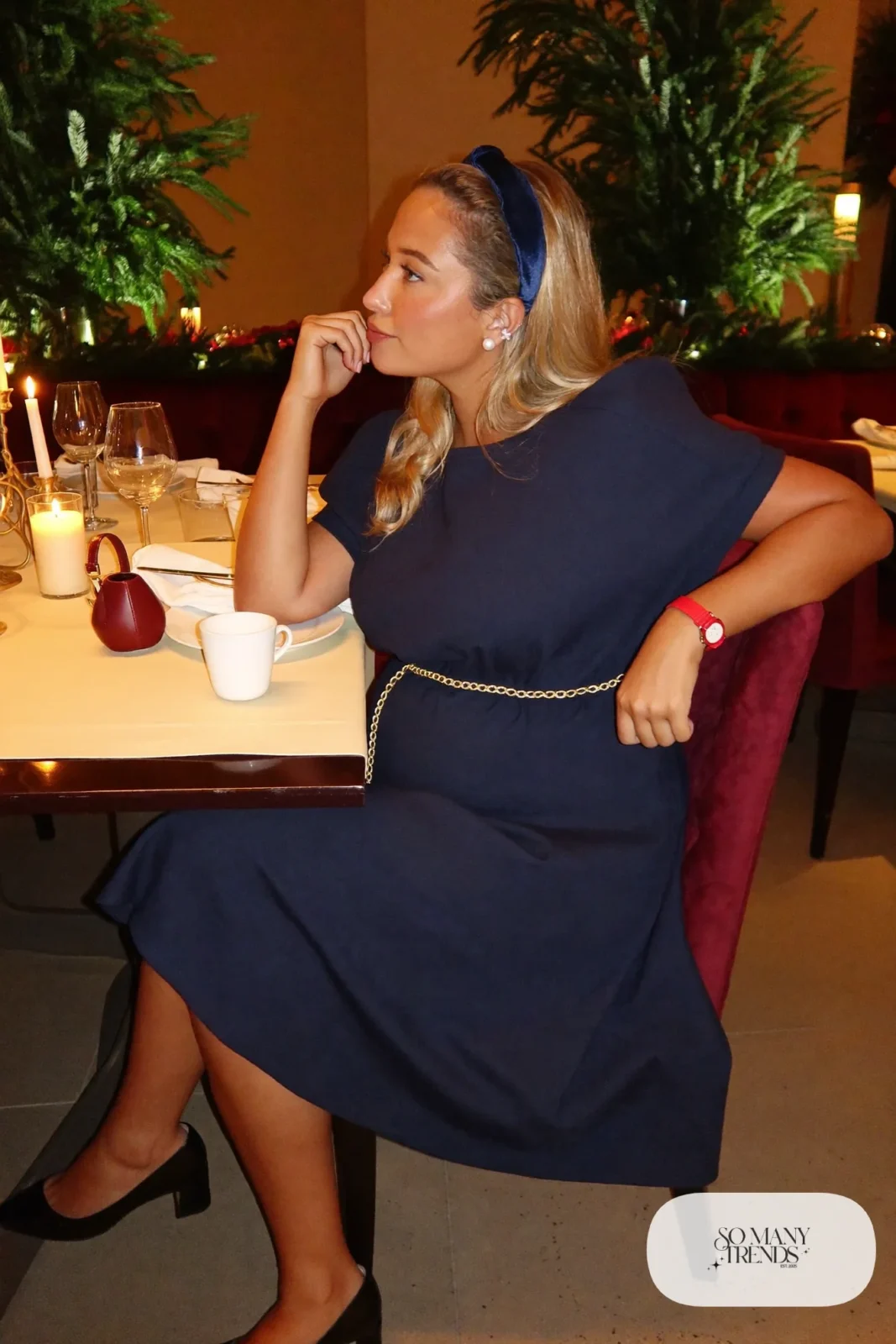 pregnant woman in navy empire waist midi dress, thin gold belt, pearl earrings, navy ribbon headband, black kitten heel pumps, small red wristlet, outfit 11